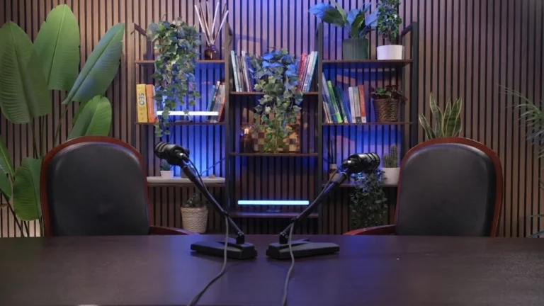 Allestimento con libreria illuminata di blu, piante e due postazioni con microfono nello studio Podbox